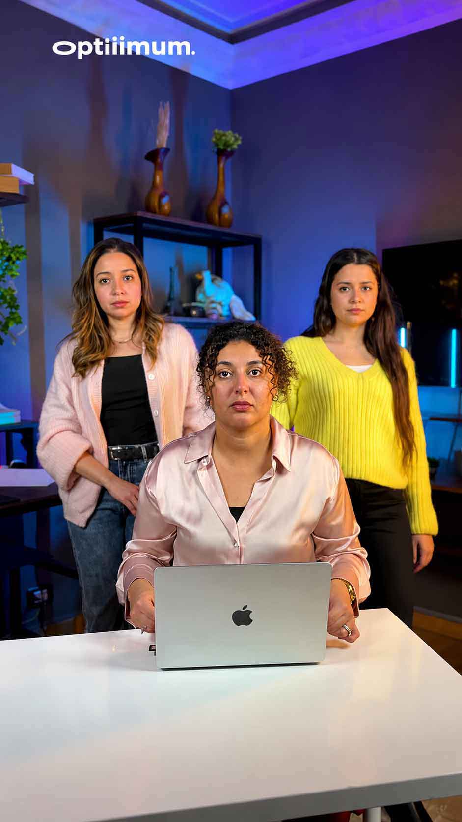 Three Optiiimum teammates on the studio set, one working on a laptop